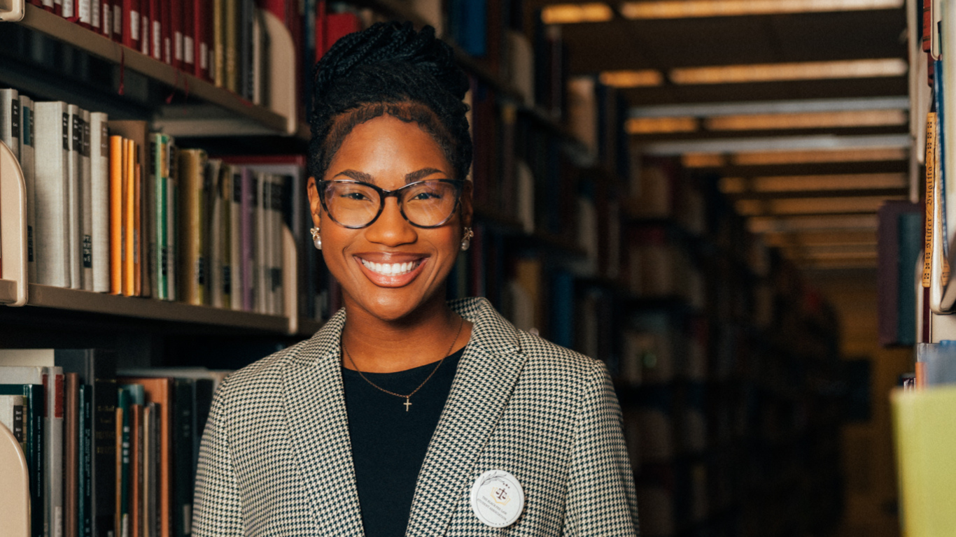 A student wearing a houndstooth blazer, smiling in the library