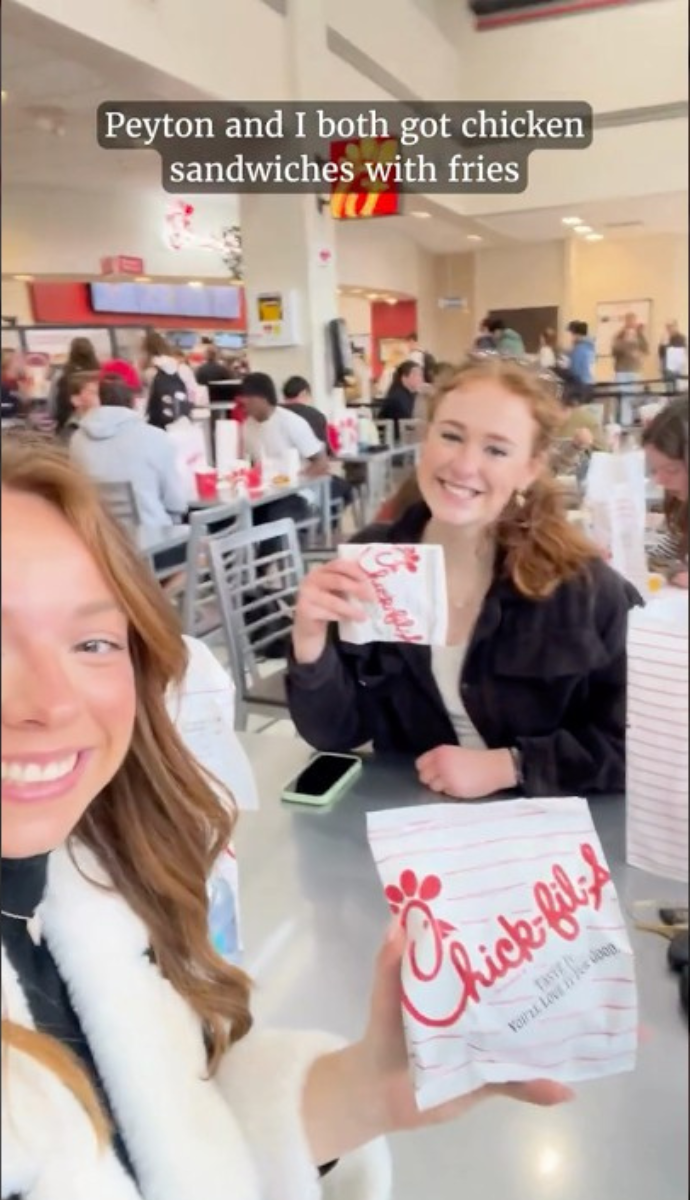 two students smiling with chicken sandwiches in hand